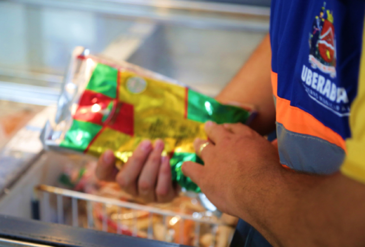 A imagem mostra uma pessoa segurando um produto embalado em uma loja, usando um uniforme azul com o nome UBERABA.